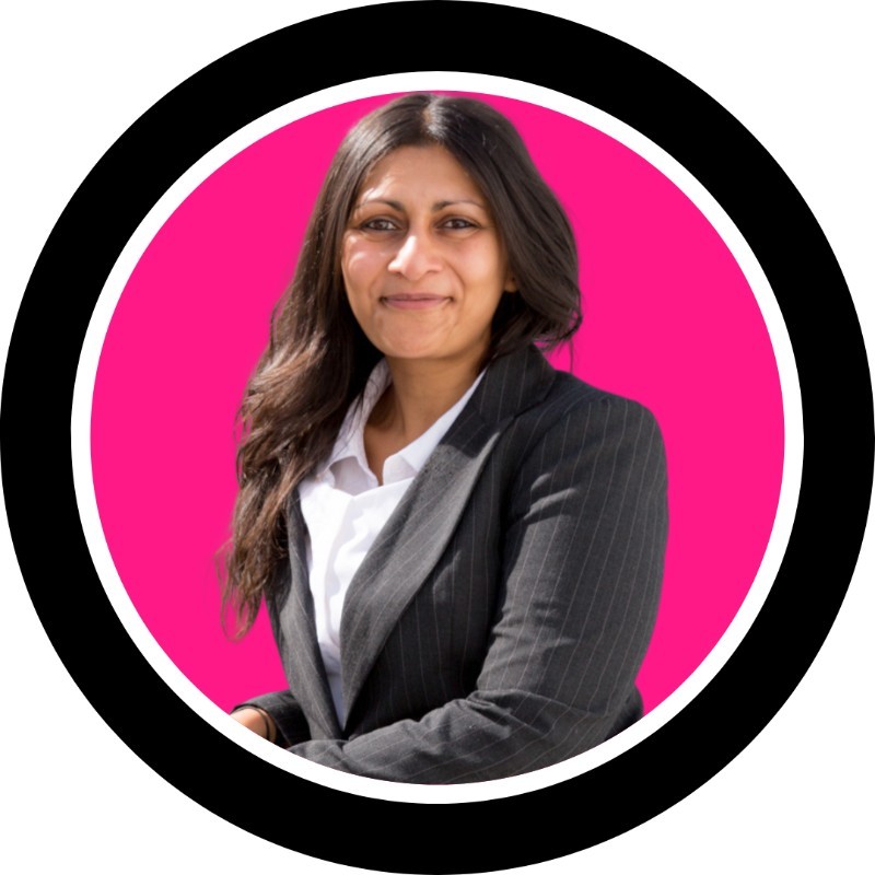 Prina Shah is a brown woman with long black hair looking confidently into the camera. Her background is hot pink and she's wearing a tailored suit.