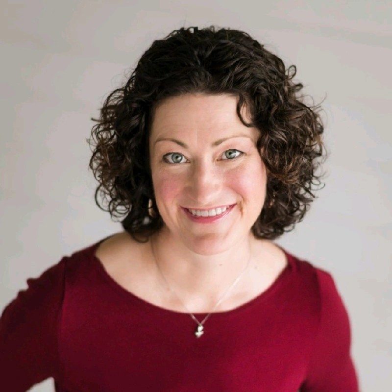 Stacey Larsen is a white woman with shoulder length curly brown hair. She's looking right at the camera with a wide smile.